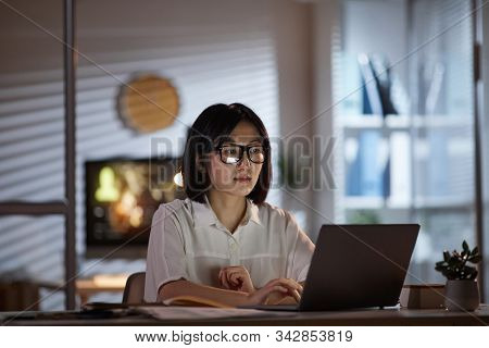 Serious Asian Businesswoman Working Online On Laptop Computer At Her Workplace Till Late At Office
