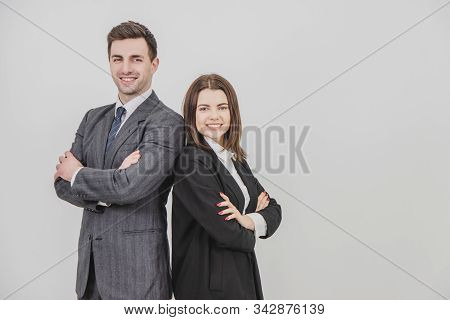 Business Man And Woman Standing Alongside, Looking At The Camera, Smiling, Their Hands Folded.