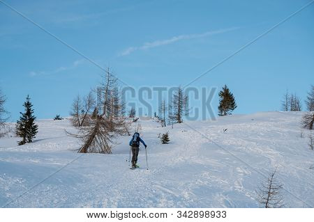 Lonely Skiier Ascending Snowy Mountain Top At Dusk.