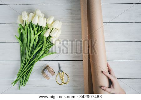 Woman Florist Wrapping Beautiful Bouquet Of White Tulips In Pack Craft Paper On The Wooden Table. Fl