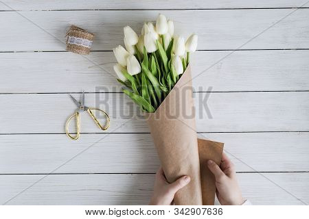 Woman Florist Wrapping Beautiful Bouquet Of White Tulips In Pack Craft Paper On The Wooden Table. Fl