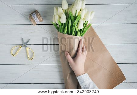 Woman Florist Wrapping Beautiful Bouquet Of White Tulips In Pack Craft Paper On The Wooden Table. Fl