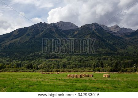 Bales Of Hay In A Farm Field With Canadian Rocky Mountains In The Background During A Vibrant Sunny 