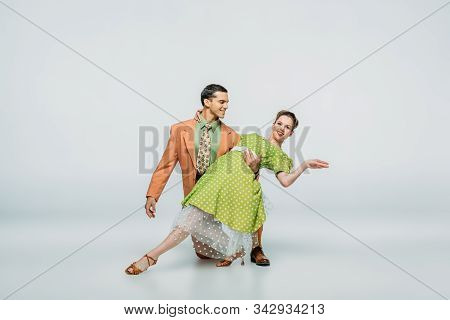 Handsome Dancer Standing On Knee And Supporting Partner While Dancing Boogie-woogie On Grey Backgrou
