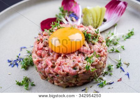 Gourmet tartar raw from beef fillet with yellow of the egg and vegetable as closeup on modern design dish 