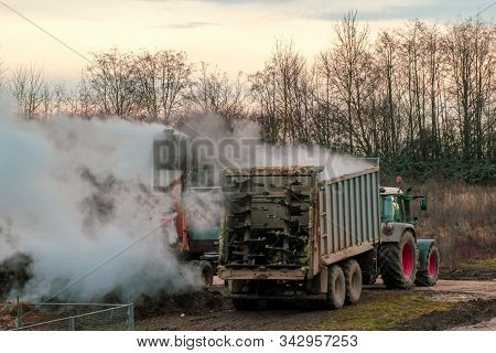 Excavator Loads Manure, Hovering In The Cold Air, Into A Tractor With A Trailer. Late Fall. Animal H