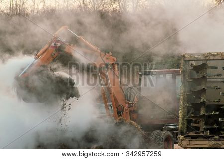 Excavator Loads Manure, Hovering In The Cold Air, Into A Tractor With A Trailer. Late Fall. Animal H