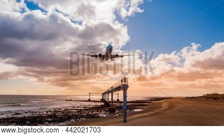Airplane Approaching Beach On Lanzarote Island, Spain. Landing Plane Over Ocean Against Sunset Sky S