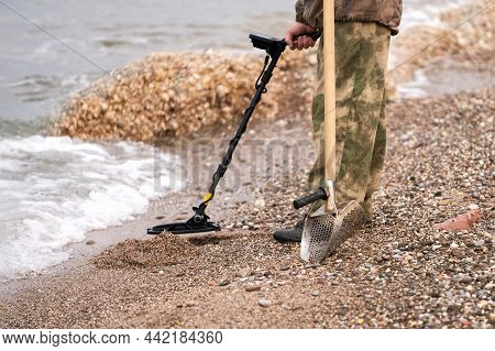 A Man With A Metal Detector And A Shovel On The Beach. Fragment. Copy Space.