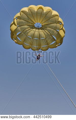 Senior White Woman With Gray Hair Is Parasailing. She Is Flying Under Yellow Parachute In Blue Sky, 