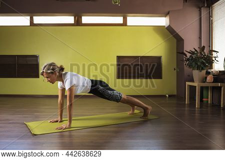 A Woman Performs The Exercise Kumbhakasana, Plank Pose, Trains In The Studio On A Mat