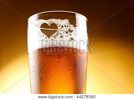 Glas bier met het hart vertegenwoordigd met schuim omhoog sluiten op gele achtergrond