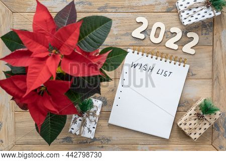 Notepad On The Wooden Background With The Inscription - Wish List. Poinsettia In The Pot, Gift Boxes