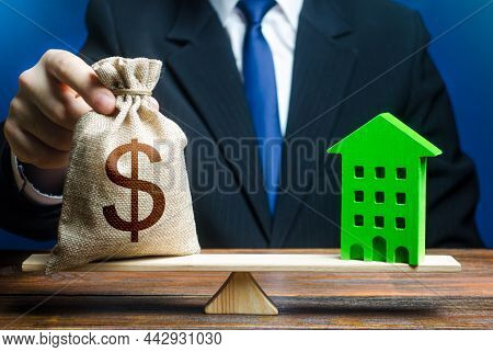 Businessman Puts Dollar Money Bag On Scales And Green House. Profitability Housing Of Eco Technologi