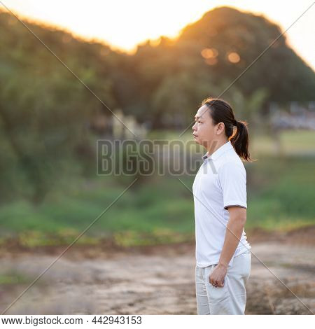 Asian Man Long Hair Stands And Relax On The Dry Field In Golden Twilight Time.