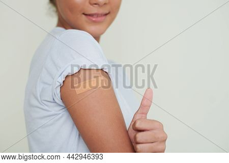 Cropped Image Of Teenage Girl With Adhesive Plaster On Her Shoulder Showing Thmbs-up After Getting V