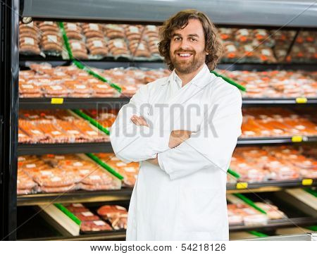 Portrait of confident salesman standing arms crossed in butcher's shop