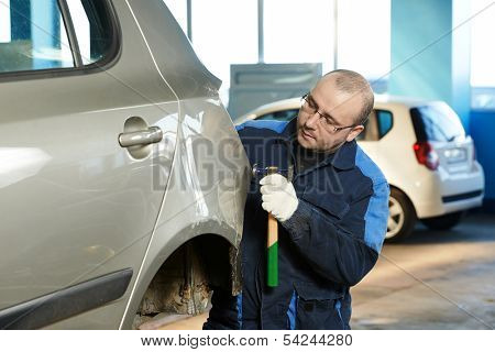 auto repair man worker flatten and align metal body car with hammer in automotive industry