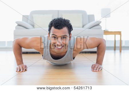 Portrait of a sporty smiling young man doing push ups in the living room at house