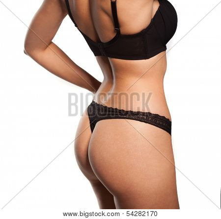 Close up view of the shapely curvaceous body of a sexy tanned young woman in black lingerie standing with her hands to her hips, torso view on white