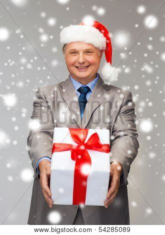 business, christmas, xmas, happiness concept - smiling old man in suit and santa helper hat with gift