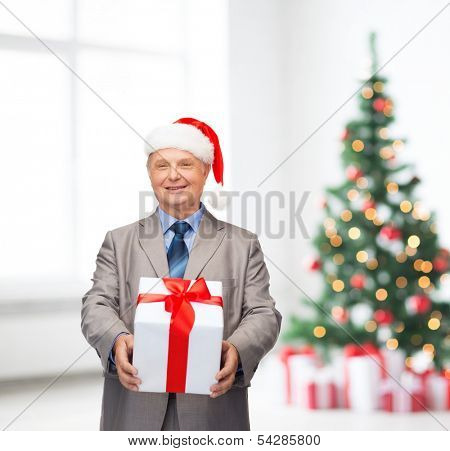 business, christmas, xmas, happiness concept - smiling old man in suit and santa helper hat with gift