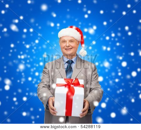 business, christmas, xmas, happiness concept - smiling old man in suit and santa helper hat with gift