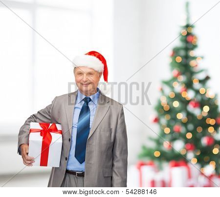 business, christmas, xmas, happiness concept - smiling old man in suit and santa helper hat with gift