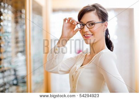 Portrait of beautiful young woman trying new glasses in optician store