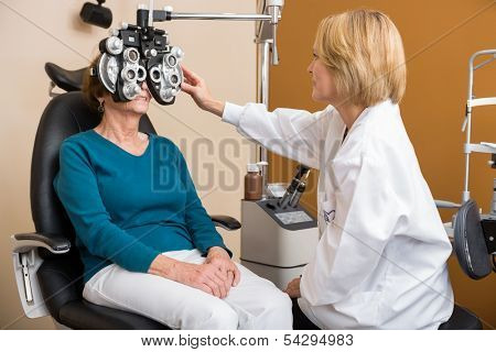 Female optician using phoropter to examine senior woman's eyes
