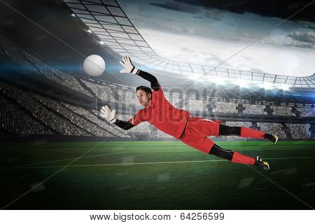 Fit goal keeper jumping up in a large football stadium with lights