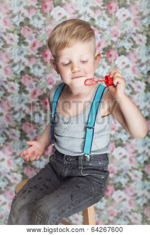 Beautiful joyful blond boy blowing soap bubbles