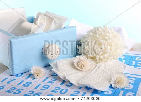 Sanitary pads in box and sanitery pads and white flowers on blue calendar on light blue background