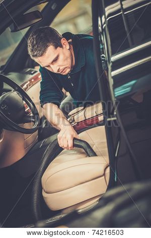 Worker on a car wash cleaning car interior with vacuum cleaner 