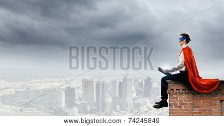 Young man in superhero costume reading book