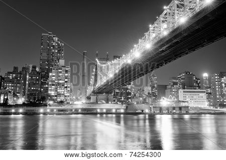 Queensboro Bridge over New York City East River black and white at night with river reflections and midtown Manhattan skyline illuminated. 