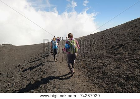 ETNA NATIONAL PARK, SICILY, ITALY - OCTOBER 18, 2014: row of hikers going down the steep path of a crater at the border with the area of high criticality of the summit south-east crater. 