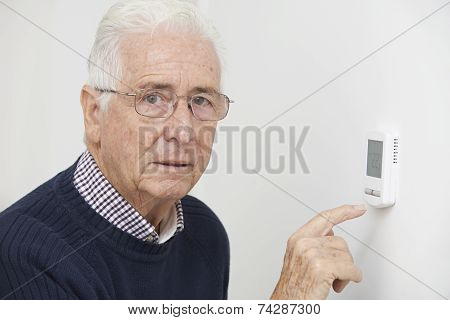Worried Senior Man Turning Down Central Heating Thermostat