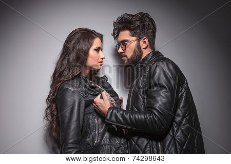 Young fashion couple face to face, the man is pulling his girlfriend leather jacket.
