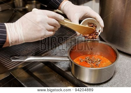 Chef is cooking the puttanesca sauce, adding chopped olives