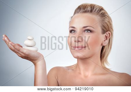 Portrait of beautiful woman holding on hand spa stones over gray background, natural cosmetics and treatment, zen balance