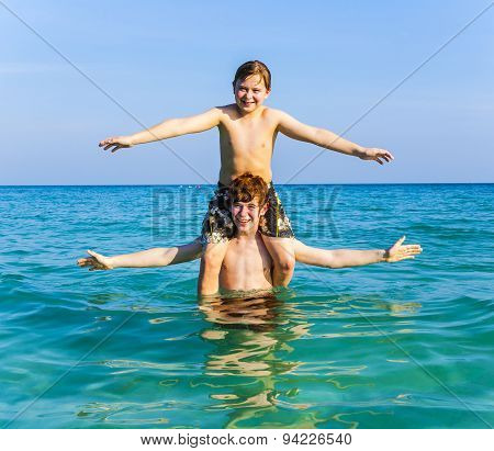 Brothers Are Enjoying The Clear Warm Water In The Ocean And Play Pickaback