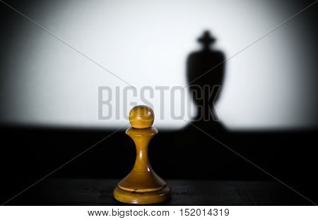 a chess pawn casting a king piece shadow in dark concept of strength and aspirations