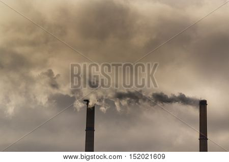 Air pollution from coal-powered plant smoke stacks, and industrial cityscape, profiled on sunset colors