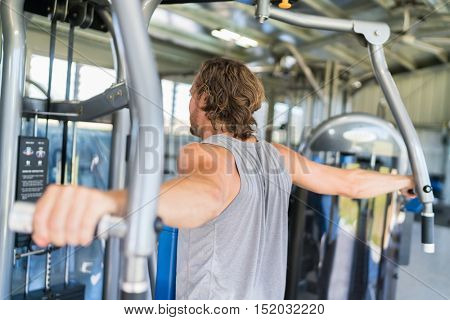 Man from behind training at fitness gym. Man doing workout on fitness machine at gym. Gym trainer athlete working out back muscles doing strength training exercises on gym  equipment.