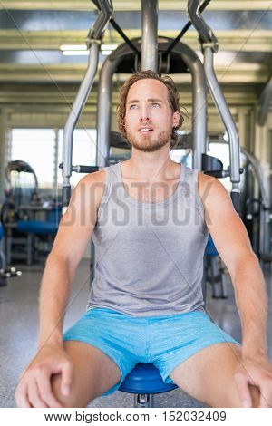 Gym fitness center workout man taking a break after workout on fitness strength training machine. Man sitting pensive after set of shoulder chest press on benchpress fitness equipment at home gym.