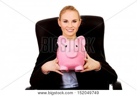 Business woman sitting on armchair and holding piggybank