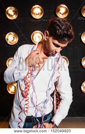Happy dark haired man in white shirt dancing at new year party. Young adult with ribbons on his shoulders.