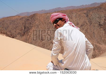 Man in bedouin clothes sitting on dune