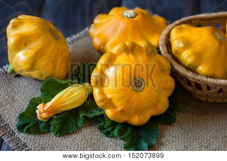 three yellow pattypan squash with leaf and flower on a dark wooden table.